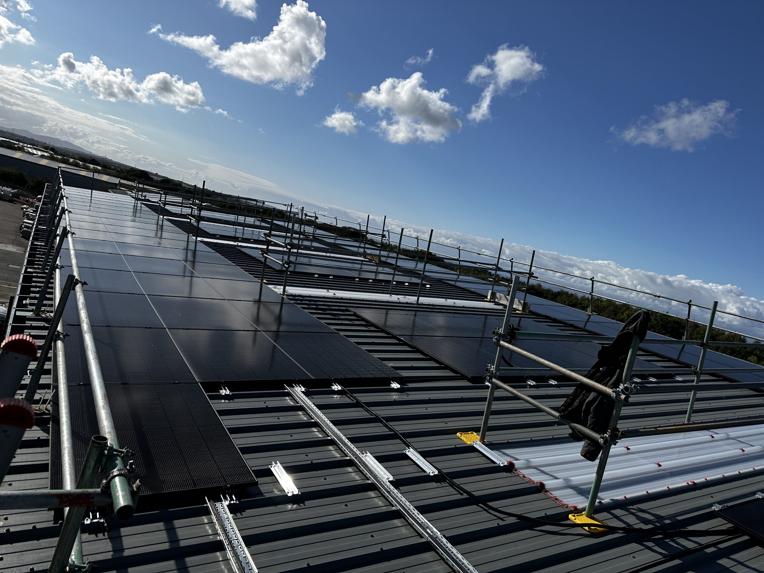 Large commercial solar panel array being installed on a metal roof in Scotland